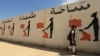 FILE - An Iraqi student walks past a school wall covered with drawings showing how Islamic State militants executed their prisoners in Mosul, Iraq, April 30, 2018.