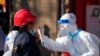 In this photo released by China's Xinhua News Agency, a worker wearing a protective suit collects a throat swab sample at a COVID-19 testing site in Xi'an in northwestern China's Shaanxi Province, Dec. 21, 2021.