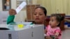 FILE - In this Sunday, Feb. 25, 2018, file photo, a woman holds a child as she casts a ballot in Kandal province, southeast of Phnom Penh, Cambodia. Cambodia's National Election Committee has warned that anyone urging voters to boycott the upcoming genera