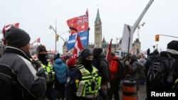 FILE - Maafisa wa polisi wakiwa na waandamanaji mbele ya jengo la Bunge wakati wenye magari na wafuasi wao wanaopinga masharti ya COVID-19 na kuchanja, Ottawa, Canada, Feb. 6, 2022.