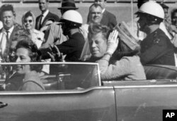FILE - President John F. Kennedy waves from his car in a motorcade approximately one minute before he was shot, Nov. 22, 1963, in Dallas.