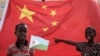 在中国资助的有千所住房单位的吉布提建筑工程启动仪式之前，拿着吉布提国旗的小男孩站在巨大的中国国旗前。（2018年7月4日） 