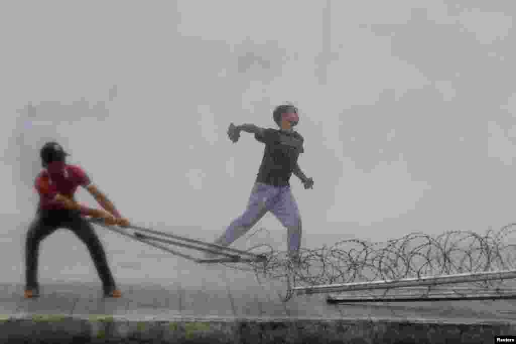 A protester supporting the opposition Cambodia National Rescue Party throws a stone as another tries to remove barbed wire barricades during clashes with police in Phnom Penh, Sept. 15, 2013.