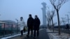 People walk along a path as the Beijing Olympic Tower is seen during a smoggy day in Beijing, Jan. 24, 2022. 