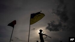 Un niño juega con un arma de plástico, bajo dos banderas nacionales, en una carretera en la región de Jarkov, Ucrania, el 20 de julio de 2022.