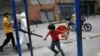 Un niño, con un tapabocas en la barbilla, juega junto a un trabajador de la ciudad que rocía desinfectante en una calle del barrio Catia, en Caracas, Venezuela.