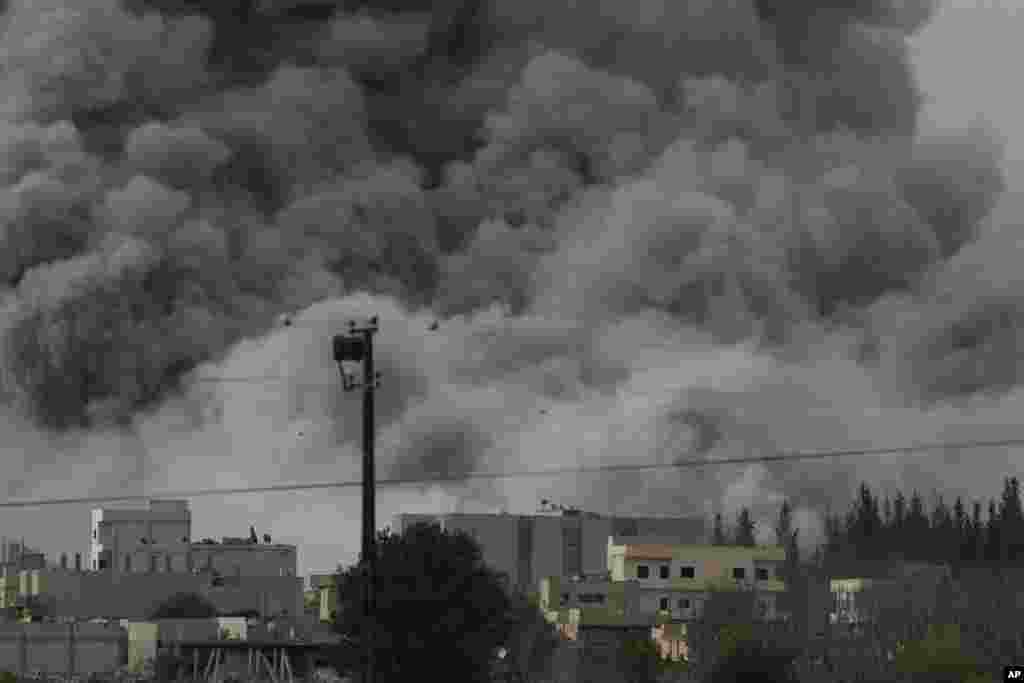 Une épaisse fumée, des débris et des flammes s’élèvent après une frappe aérienne de la coalition menée par les Etats-Unis à Kobani, en Syrie alors que des combats s’intensifient entre les Kurdes Syriens et des combattants de l’Etat Islamique, comme observé depuis le faubourg de Suruc, à la frontière Turco-Syrienne, dimanche le 12 octobre 2014. (AP Photo/Lefteris Pitarakis)
