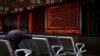 FILE - An investor takes a nap in front of an electronic board displaying stock prices at a brokerage house in Beijing, Monday, Sept. 17, 2018.