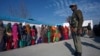 Voters line up to cast their votes as an Indian security officer stands guard outside a polling station during the last phase of the Jammu and Kashmir state assembly elections on the outskirts of Jammu, Dec. 20, 2014.