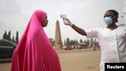 Mhudumu wa afya nchini Nigeria apima joto la mwanamke ili kubaini iwapo huenda anaugua.