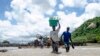 FILE - People cross a river with their belongings where a bridge once stood in Phaloni, Southern Malawi, Jan 22, 2015.