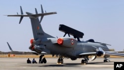 Engineers and support staff sit in the shade of an Embraer EMB-145I aircraft fitted with the India's first indigenous airborne radar system during rehearsals for the Aero India 2015 at Yelahanka air base in Bangalore, India, Feb. 17, 2015.