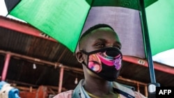 Mchuuzi katika soko la Nakasero mjini Kampala Uganda akiwa amevaa barakoa na kushika mwamvuli.(Photo by SUMY SADURNI / AFP)