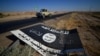 FILE - A black sign belonging to Islamic State militants is seen on the road in Al-Fateha military airport south of Hawija, Iraq, Oct. 2, 2017. Remaining IS fighters in Iraq and Syria are fleeing for parts of Syria controlled by President Bashar al-Assad. 