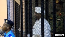 Rais wa zamani wa Sudan Omar Hassan al-Bashir akiwa mahakamani kwenye kizuizi cha vyuma akikabiliwa na mashtaka ya ufisadi, Khartoum, Sudan, Aug. 19, 2019.
